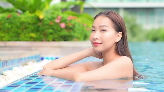 An attractive young woman in a swimming pool leans up along the edge of a posh resort swimming pool. 