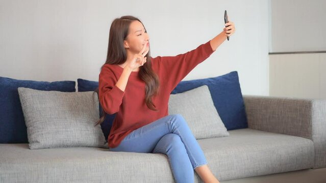 Finding the right selfie pose is hard work for an attractive young woman sitting on a modern couch.