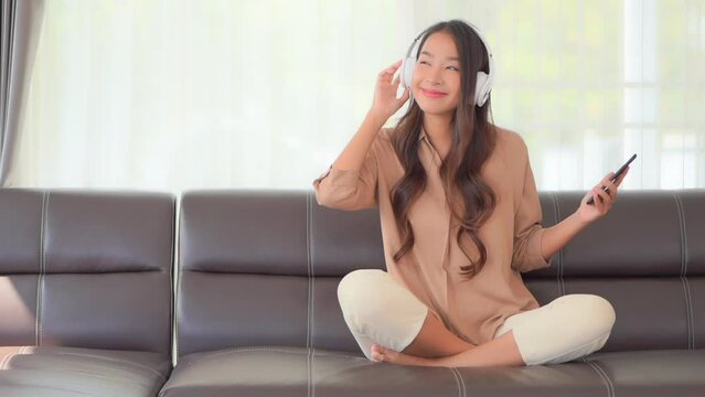 A cute young woman sits crossed-legged on the couch as she moves to the rhythm of the music playing through her headphones.  Title space
