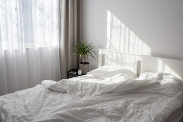 Minimalistic modern bedroom with white bedding and grey curtains. Morning light from the window...