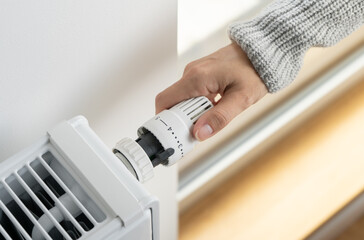 A woman adjusts the radiator thermostat to the economical mode of room heating - obrazy, fototapety, plakaty