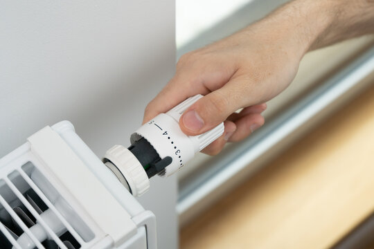 The man adjusts the radiator thermostat to the economical mode of room heating