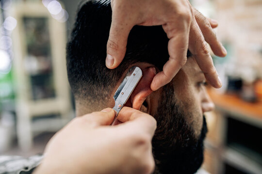 Crop barber cutting hair of client with razor