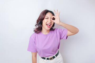 Obraz na płótnie Canvas Excited Asian woman wearing a lilac purple t-shirt giving an OK hand gesture isolated by a white background