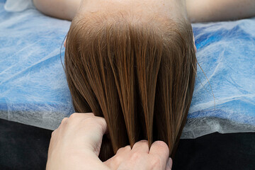 A young Caucasian girl with brown hair lies on a head massage procedure in a beauty salon.