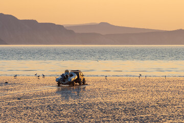 At low tide, an off-road car carries an inflatable rubber boat along the shallows to the sea....
