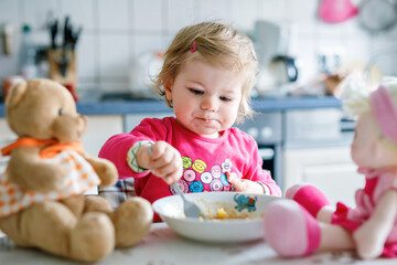 Obraz na płótnie Canvas Adorable baby girl eating from fork vegetables and pasta. food, child, feeding and development concept. Cute toddler, daughter with spoon sitting in highchair and learning to eat by itself.