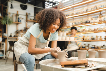 Creative afro American young woman artist molding clay on pottery wheel, Workshop in ceramic studio, clay making of a ceramic pot on the pottery wheel, hobby and leisure with pleasure concept