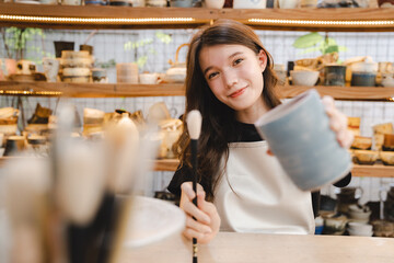 Beautiful young woman holding pottery instrument for scraping, smoothing, shaping and sculpting. Lady siting on bench with pottery wheel and making clay pot