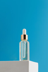 A transparent glass dropper with a cosmetic product on a podium on a blue background.