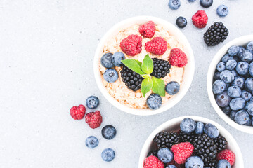 Healthy breakfast - bowls with oatmeal porridge served with various berries on concrete table background with copy space. Morning superfood porridge recipe