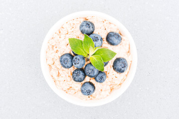 Healthy breakfast - oatmeal porridge served with blueberry and mint leaves on concrete table background. Morning superfood porridge recipe