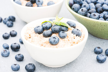 Oatmeal porridge served with blueberry and mint leaves on concrete table background. Morning superfood porridge recipe. Healthy breakfast ideas