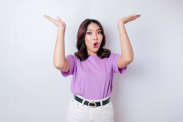 Fototapeta na wymiar Shocked Asian woman wearing lilac purple t-shirt pointing at the copy space upside her, isolated by white background