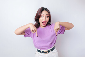 Obraz na płótnie Canvas Shocked Asian woman wearing lilac purple t-shirt pointing at the copy space downside her, isolated by white background