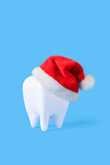 creative medical dental tooth dent in red santa hat on blue winter background. dental holiday christmas. happy new year in dentistry. Health care, hygiene concept. Copy space, vertical