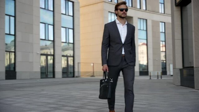 Successful confident stylish handsome caucasian businessman walking on street against background office building.