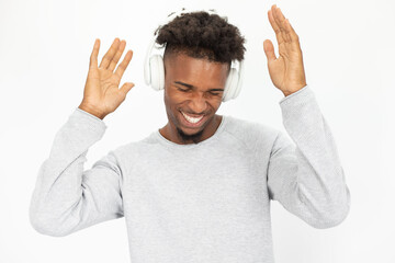 Portrait of joyful African American man listening to music in headphones. Young bearded guy wearing white sweater dancing to music against white background. Hobby and music concept