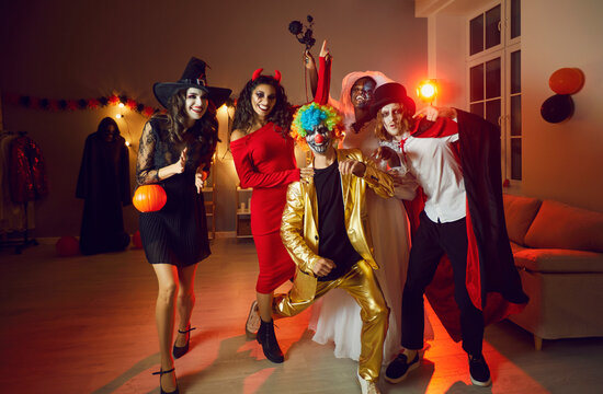 Halloween theme. Portrait of multiracial adult friends in spooky costumes having fun at Halloween party. People in images of spooky characters smile and fool around in dark room with red lights.