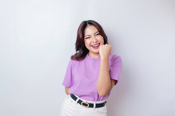 A young Asian woman with a happy successful expression wearing lilac purple shirt isolated by white...