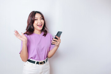 Naklejka premium A portrait of a happy Asian woman is smiling and holding her smartphone wearing a lilac purple t-shirt isolated by a white background
