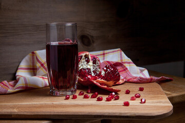 Fresh red pomegranate and glass of fresh rudy juice on a wooden background.. - obrazy, fototapety, plakaty