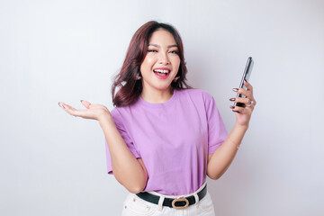 A portrait of a happy Asian woman is smiling and holding her smartphone wearing a lilac purple t-shirt isolated by a white background