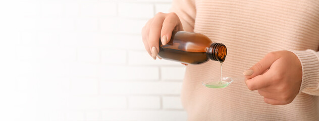 Woman pouring cough syrup from bottle into spoon, closeup. Banner for design