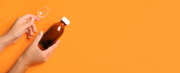 Female hands holding bottle of cough syrup and spoon on orange background with space for text - obrazy, fototapety, plakaty