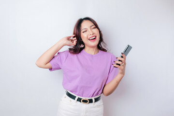 Fototapeta premium A portrait of a happy Asian woman is smiling and holding her smartphone wearing a lilac purple t-shirt isolated by a white background