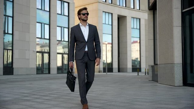 Successful confident stylish handsome caucasian businessman walking on street against background office building.