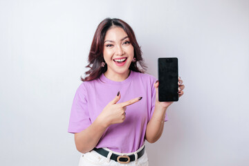 A portrait of a happy Asian woman is smiling and showing copy space on her smartphone wearing lilac purple shirt isolated by a white background
