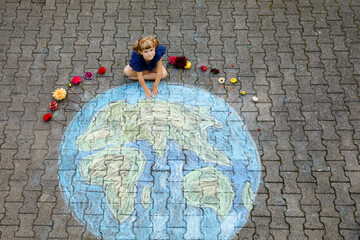 Little preschool girl with flowers and earth globe painting with colorful chalks on ground. Positive toddler child. Happy earth day concept. Creation of children for saving world, environment ecology.