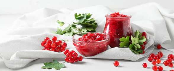 Bowl and jar of tasty red currant jam on light background