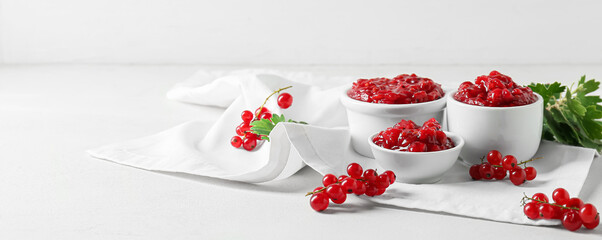 Bowls of tasty red currant jam on light background