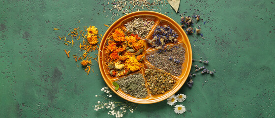 Plate with various dried flowers on green background, top view