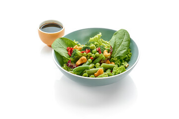 Green salad with asparagus, broccoli and walnuts in a bowl on a white background.
