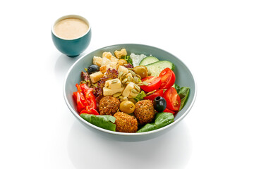 Salad with falafel, olives and tomatoes in a bowl on a white background.