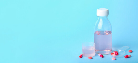 Bottle of cough syrup and pills on blue background with space for text