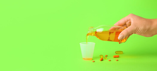 Female hand pouring cough syrup from bottle into cup on green background with space for text