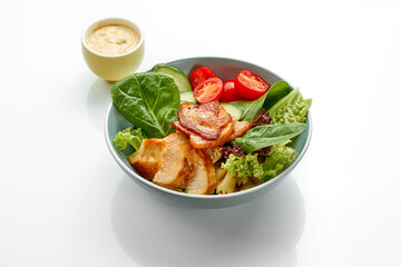 Salad with chicken, bacon and tomatoes in a bowl on a white background.