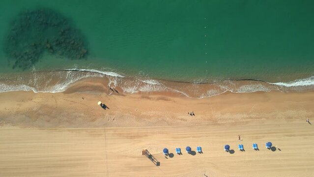 Aerial shot over a beach of yellow sand and transparent turquoise water in Malgrat de Mar, province of Barcelona Flight over hammocks and deckchairs