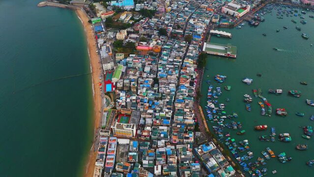 Drone shot traveling backward of a city built on an isthmus with an harbor and a popular beach