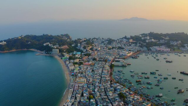 Drone shot traveling forward above a city built on an isthmus with an harbor and a popular beach during golden hour