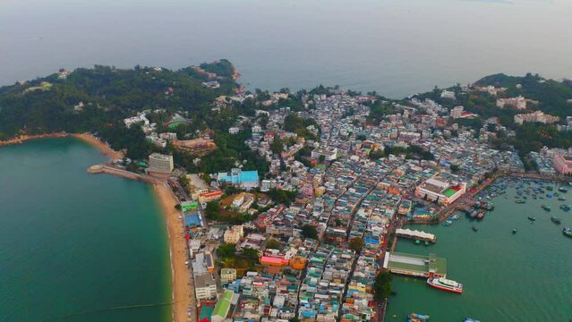 Drone shot traveling backward of a city built on an isthmus with an harbor and a popular beach during the day