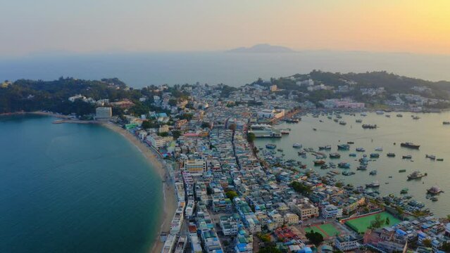 Drone shot traveling to the right above a city built on an isthmus with an harbor and a popular beach during golden hour