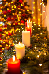 Vertical shot of line of burning candles in decorated room, Christmas tree on the background. Festive warm atmosphere at home