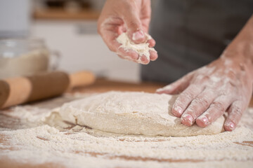 Women's hands pouring flour into raw dough while kneading bread dough on a table full of flour in the bakery kitchen
