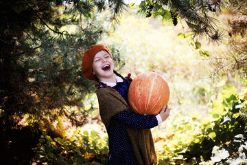 Dziewczynka w berecie i jesiennych barwach trzyma wielką dynię - obrazy, fototapety, plakaty