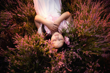 Dziewczynka leży na polanie pełnej różowych wrzosów